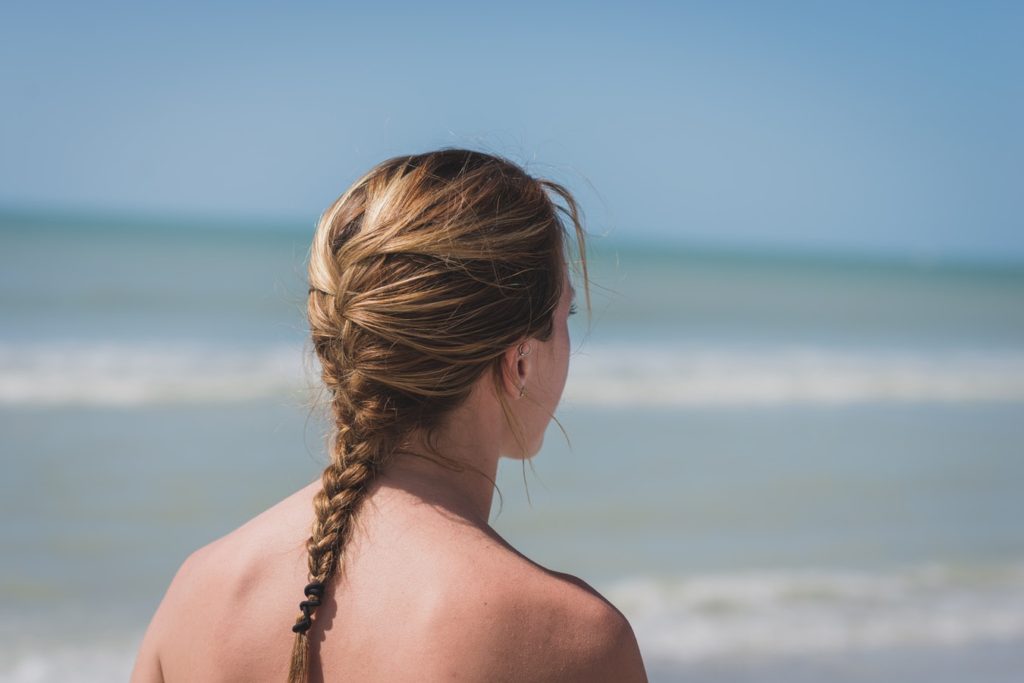 A brunette woman with a french braid hairstyle staring out into the ocean on a sunny day.