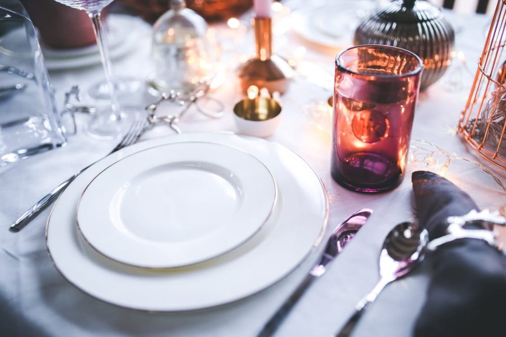 Place setting at a table including white linens, white plates, shiny silverware and a candle for ambiance.