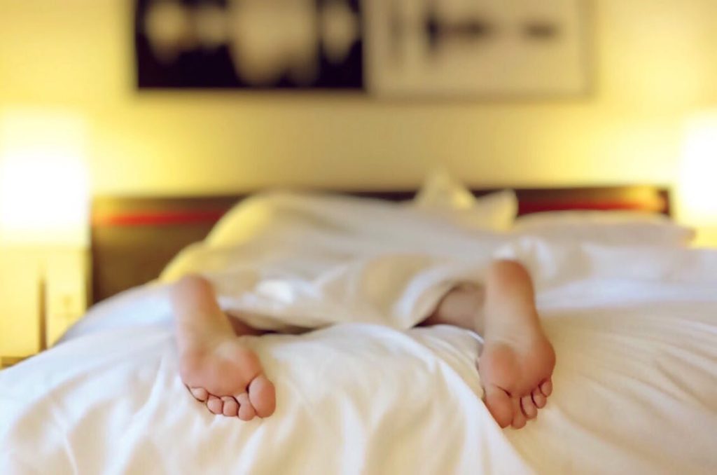 A person face down under the covers with feet sticking out at the bottom of the bed, sleeping. 