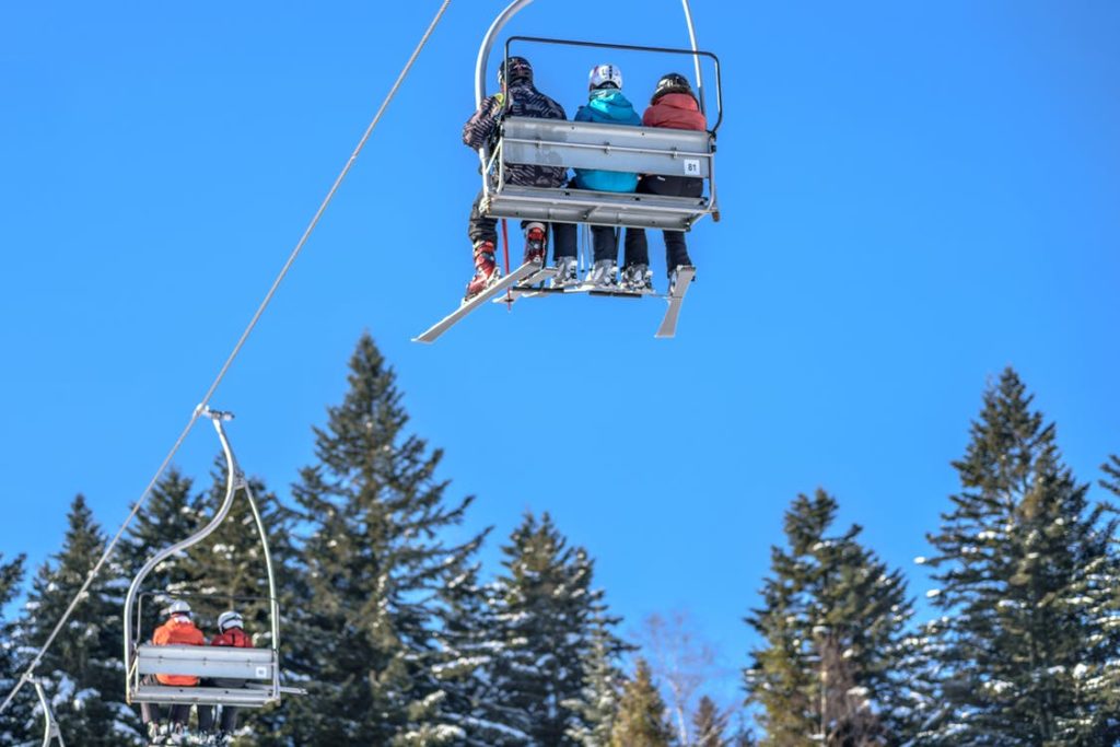 Three people sitting on the ski lift heading up the mountain. 