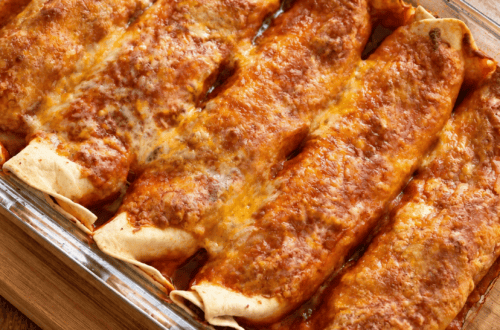 A glass pan of freshly bakes 2 point Weight Watchers enchiladas sits on a cutting board on a kitchen counter.
