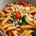 Copycat Noodles and Company Pasta Fresca with penne pasta, tomatoes, spinach, red onion, garlic, and feta cheese in a bowl.