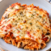 Cheesy baked spaghetti with tomato sauce, mushrooms, and melted Parmesan and mozzarella cheese in a ceramic dish, garnished with fresh parsley.