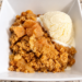 A serving of apple crisp and vanilla ice cream sit in a white bowl on a counter.