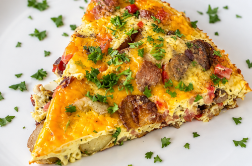 A slice of easy ham and potato breakfast bake topped with parsley sits on a white plate.