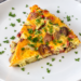 A slice of easy ham and potato breakfast bake topped with parsley sits on a white plate.