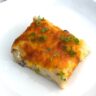 Weight Watchers Mashed Potato Bake topped with scallions sits on a white plate on a counter.