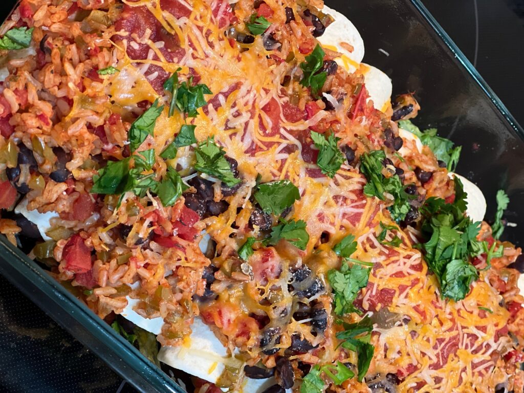 Smothered burritos topped with cheese and cilantro in a glass pan.