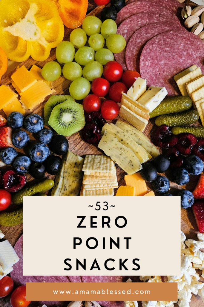 A board of various snacks such as cheese, fruit, and meat sits on a table. 