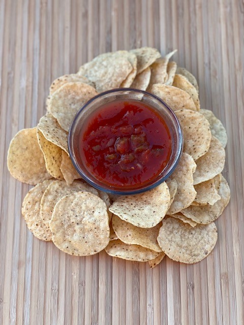 A small bowl of salsa surrounded by round tortilla chips