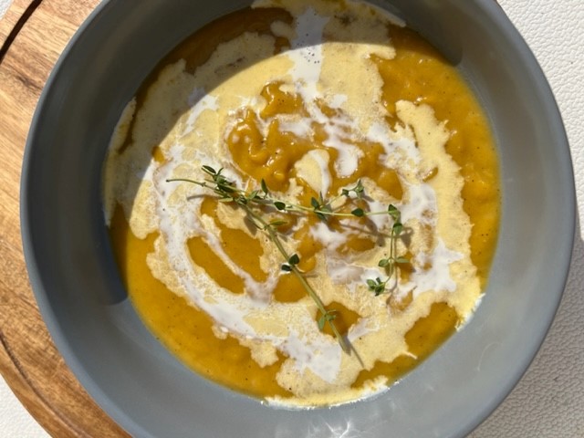 A bowl of butternut squash soup topped with a sprig of thyme,