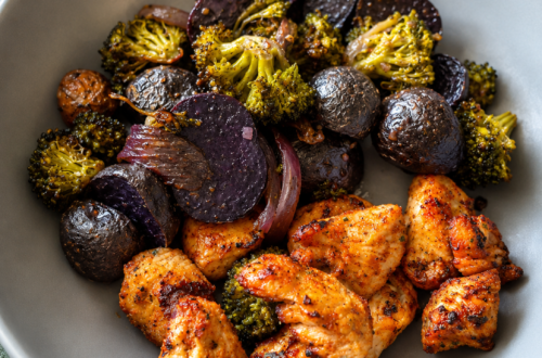 Crispy air fryer chicken and roasted broccoli, mushrooms, onions, and purple potatoes in a grey bowl on a counter.