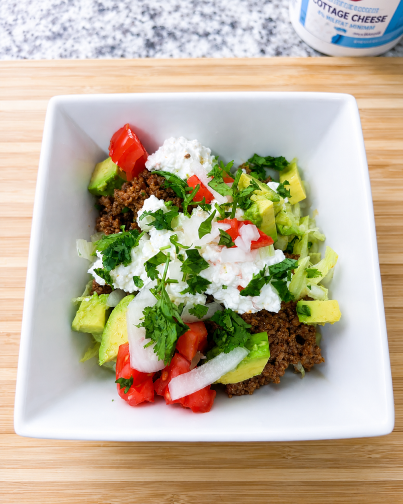 A taco bowl sits upon a wooden cutting board. 