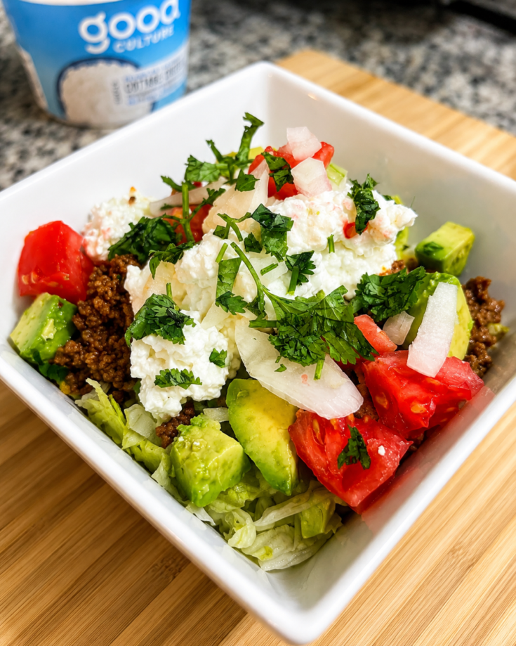 A taco bowl sits on top of a cutting board on a counter.
